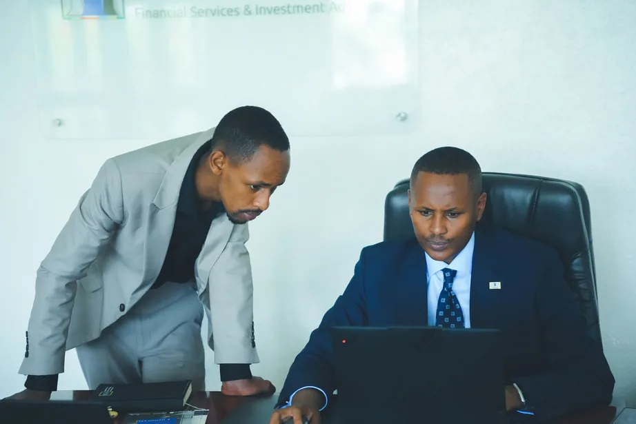 Two men in business attire reviewing documents on a laptop in an office